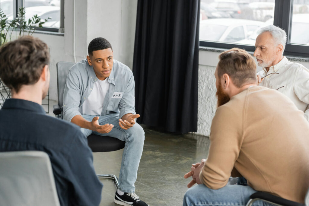 a group of men in a circle discussing the benefits of group therapy together